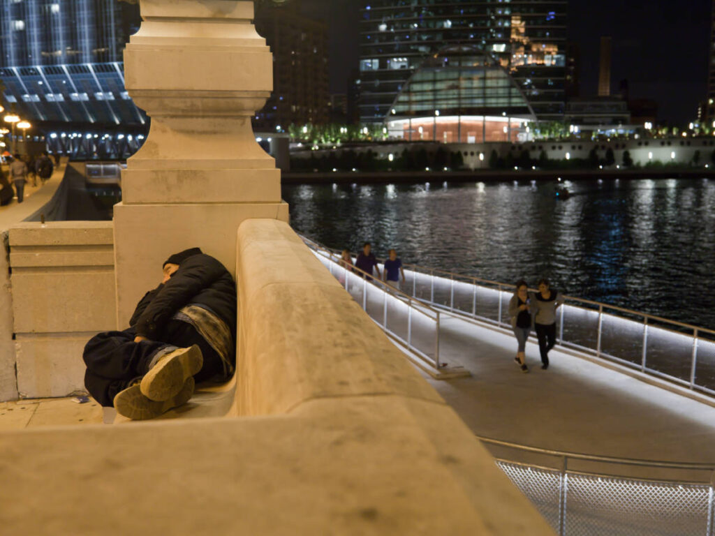 A homeless person sleeping on a public bench at night