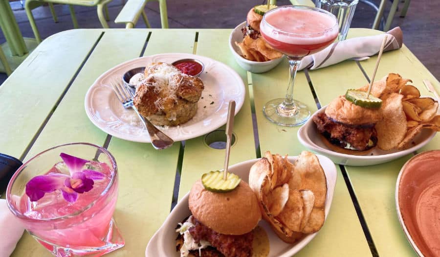 A table full of a variety of food, monkey bread, chicken sandwiches, and delicious cocktails from Honey Salt.