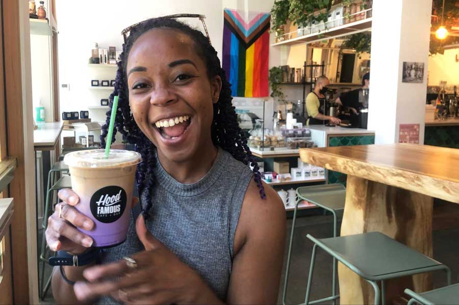 The author holding a cup of ube latte with straw in Hood Famous Cafe + Bar