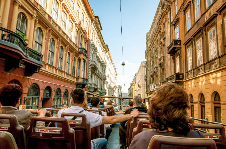 View of passengers on top of a bus surrounded by buildings in downtown Budapest