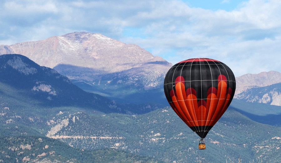View of a hot air balloon up in the sky of Colorado Springs and mountains on the backgorund
