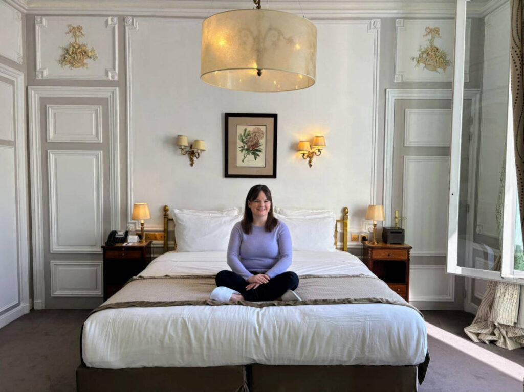The author Rachel Kapelke-Dale sitting on her bed in Hotel Regina Louvre