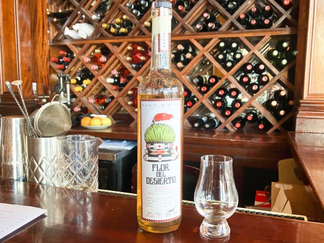 A bottle of Housemade Sotol with a wine cellar in the background