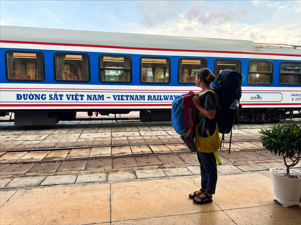 A woman carrying multiple bags in front of a train
