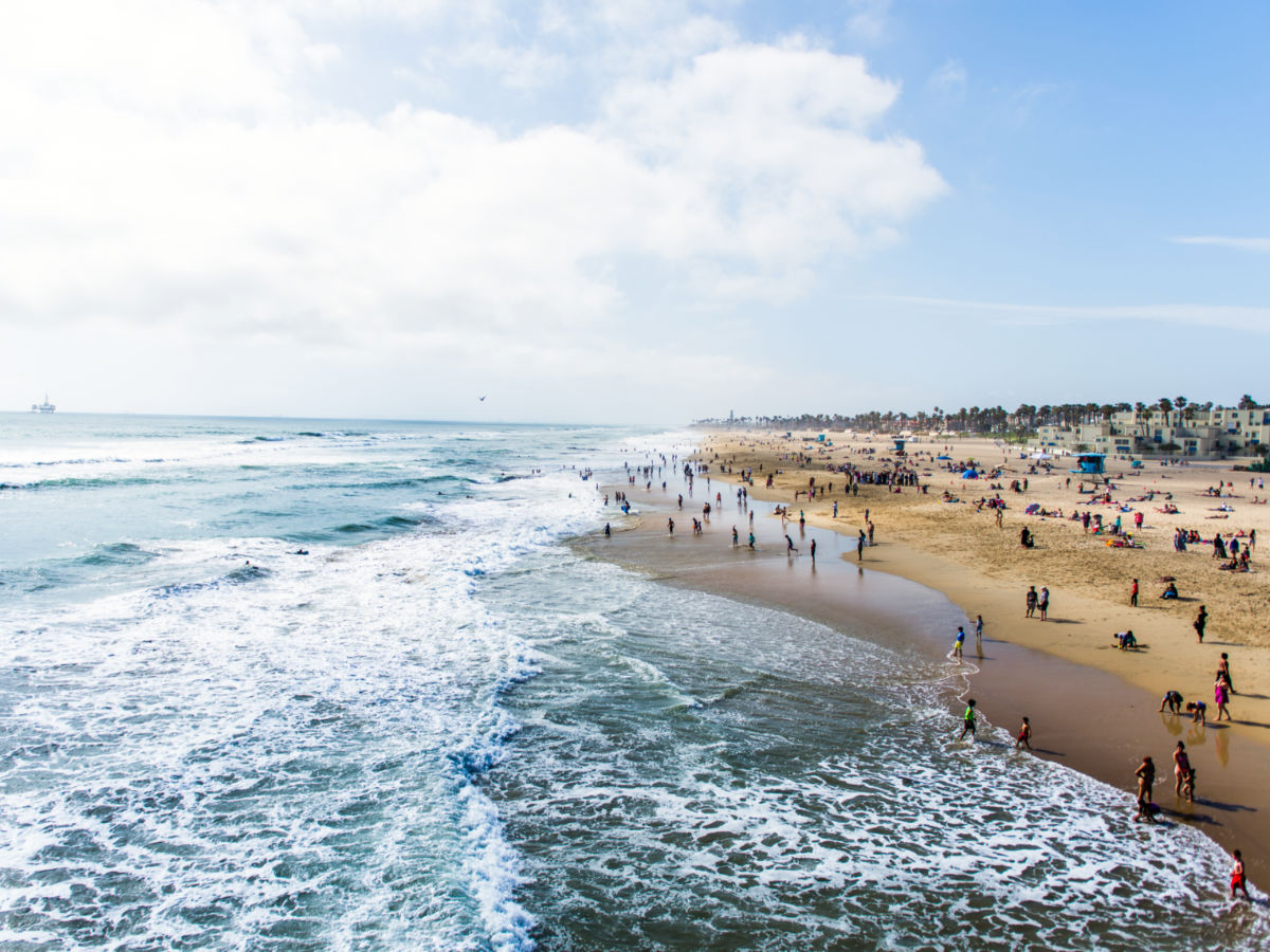 Crowds of tourists and sun bathers having fun and swimming at Huntington Beach