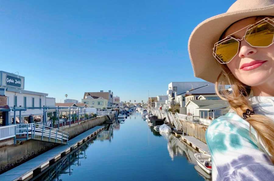 The author smiling for a selfie with the Huntington Harbor on her background