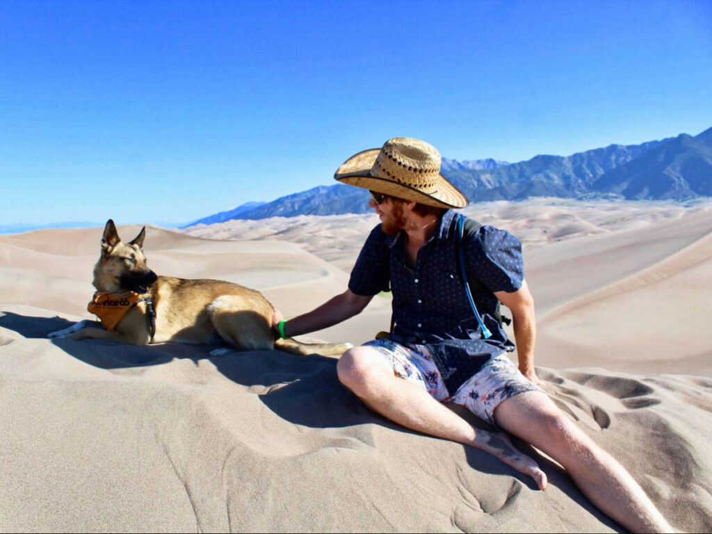 The author Abigail Bliss's husband with their dog, sitting on the High Dune summit in Great Sand Dunes National Park