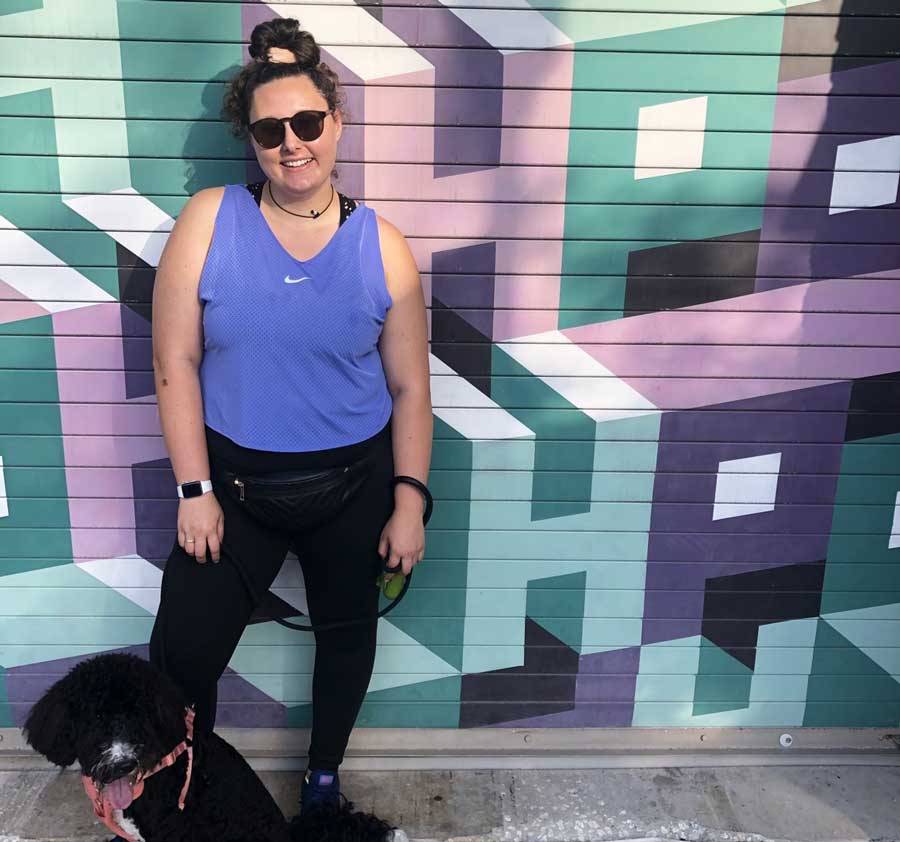 The author Marina Martinelli and her dog posing in front of a mural in Hyde Park Village