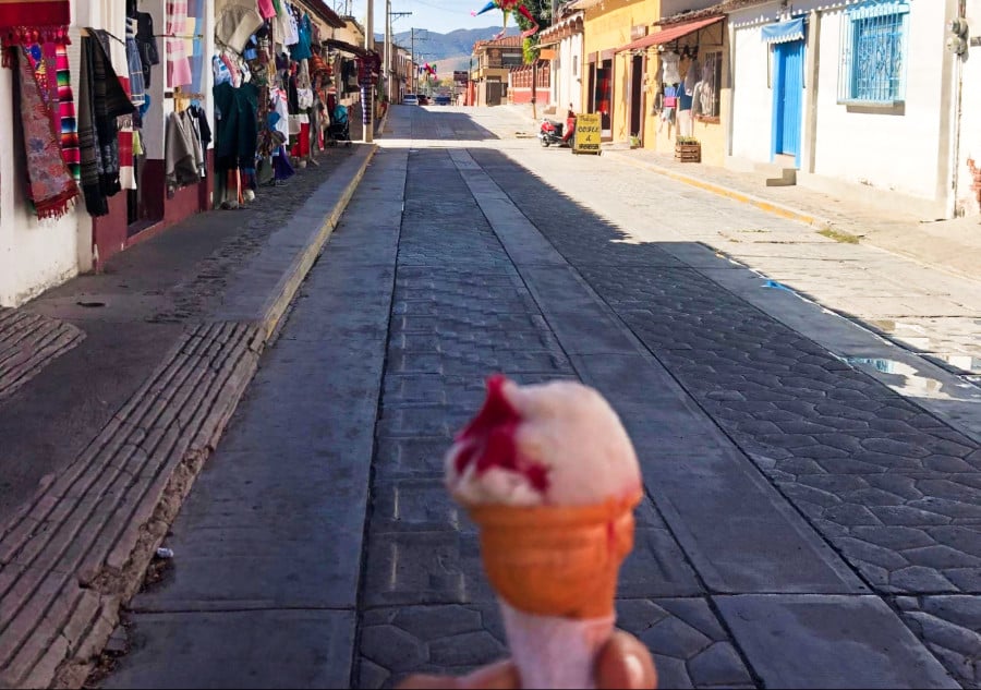 A closeup look of a hand holding an ice cream in a cone in the middle of an empty street