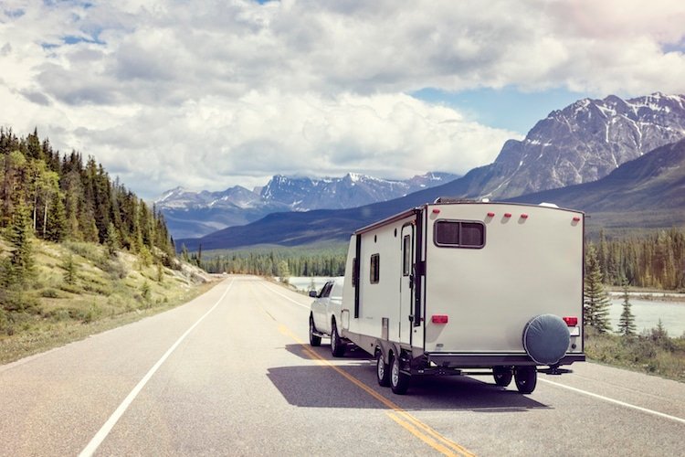 A truck hauls a camper along the Icefields Parkway in Alberta, surrounded by mountains and lakes.