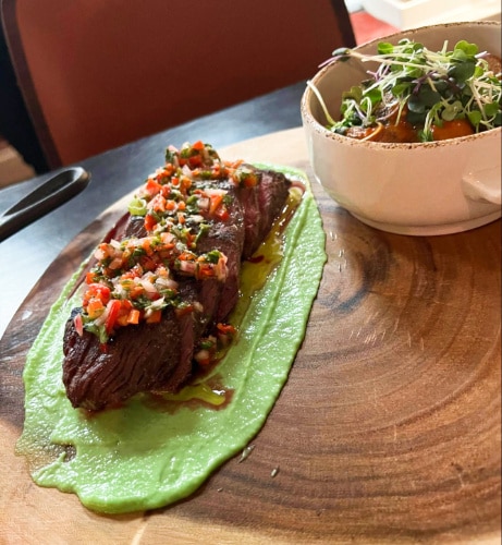 A gourmet with green sauce and a bowl of salad served on a wooden board