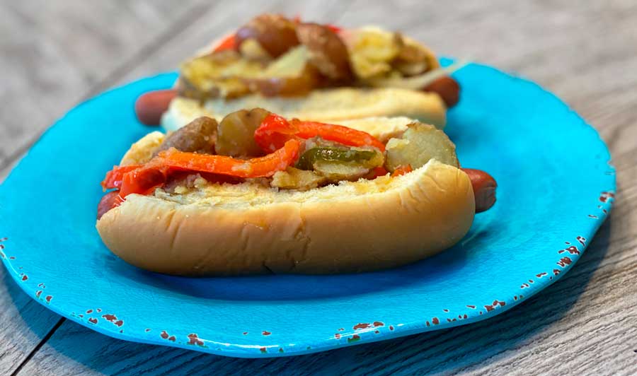 Two Italian hot dog with peppers, onions, and potatoes on a blue plate