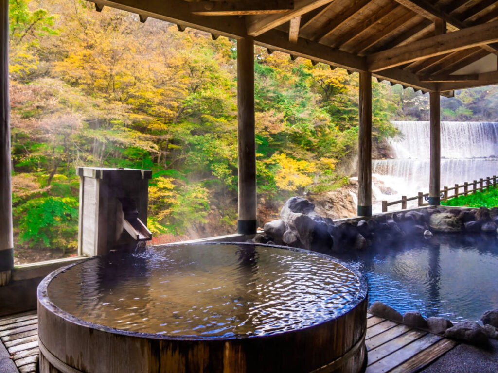 A steaming Japanese Onsen with an overlooking view of the waterfalls and the fall foliage around