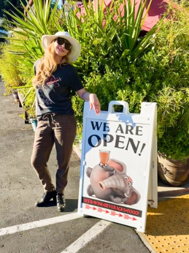 The author Jericha Griffin, posing beside the outdoor signage of The Elephant in the Room
