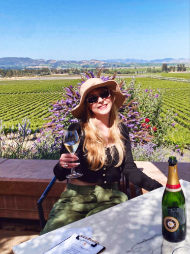 The author Jericha Griffin holding a wine glass with a scenic view of the vineyard in the background