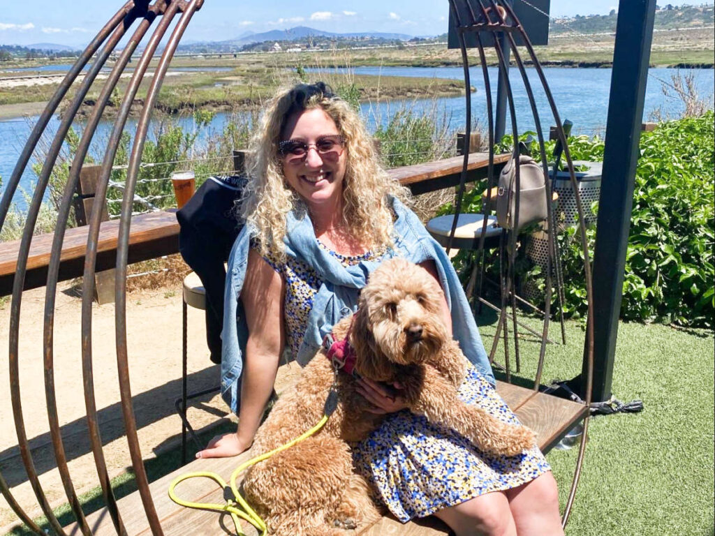 The author Jess Levy with her dog sitting on a trendy swing by the lagoon on a sunny day