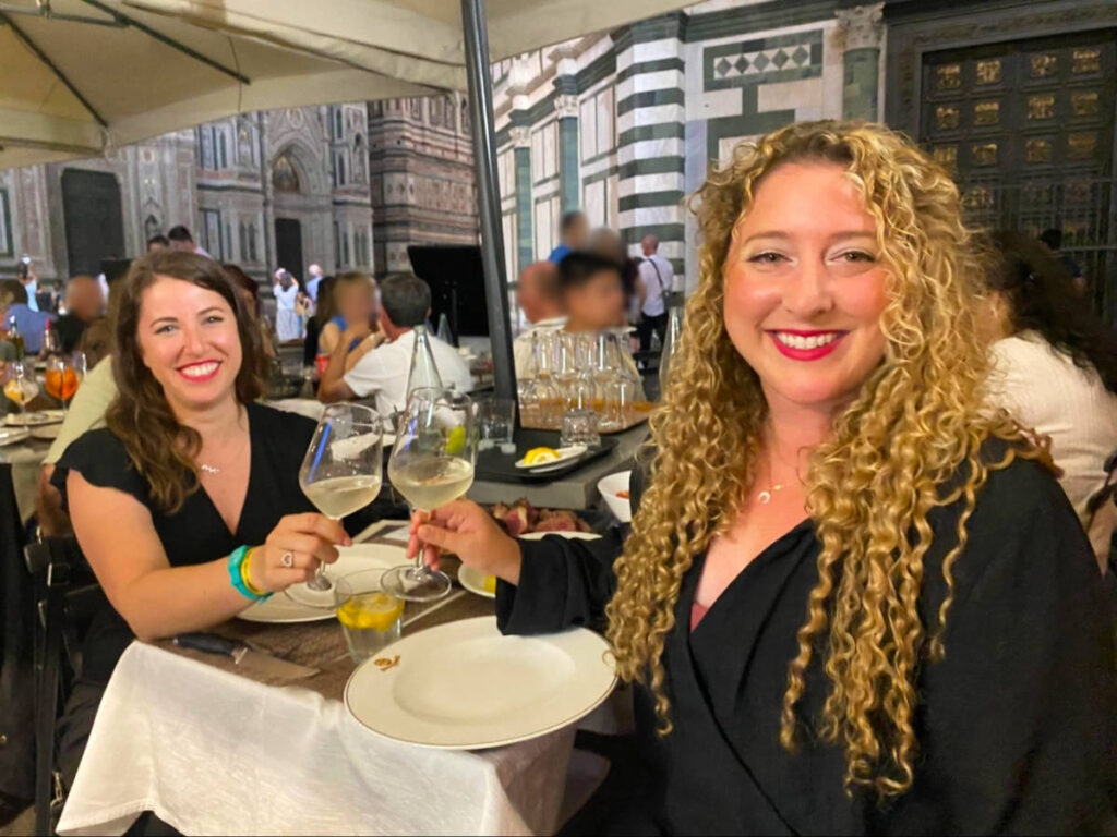 The author Jess and her friend clinking wine glasses while dining al fresco