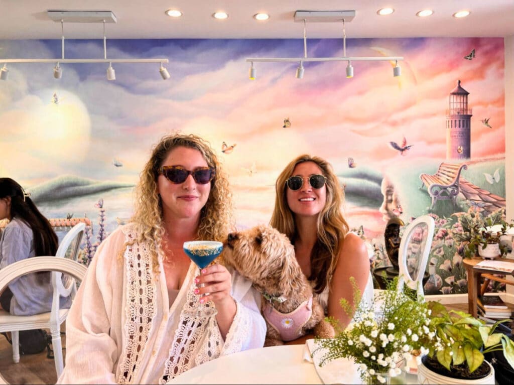 The author Jess Levy holding a glass of drink with her dog and friend at Elixir De La Lune