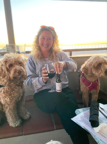 The author Jess Levy holding a drink with the dogs on both sides