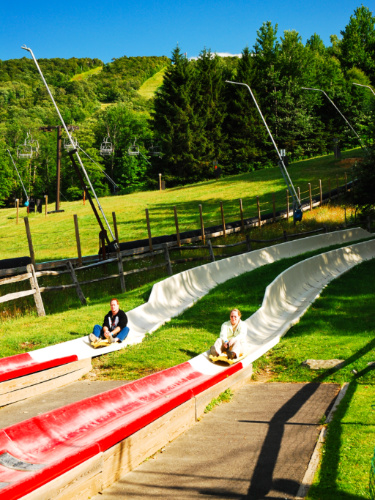 Two people sliding down at Jiminy Peak Alpine Slide on a sunny day