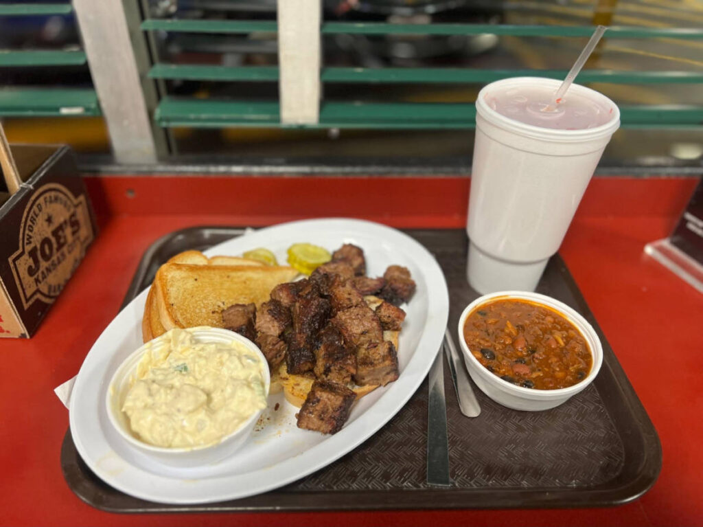 A plate of barbeque with toasted bread, side dishes and a cup of drink