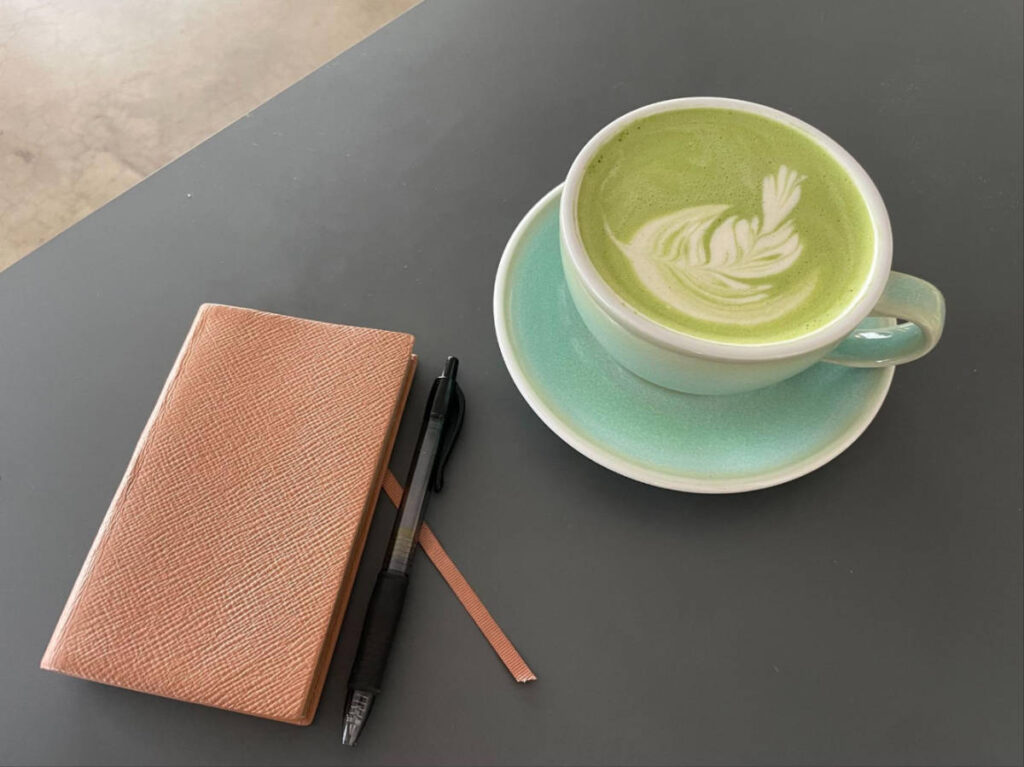 A journal, pen, and a cup of matcha latte on a table