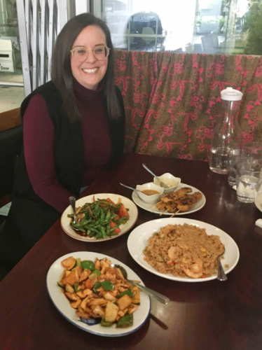 The author Catherine Driver smiling for a photo with foods on the table served in Kari House