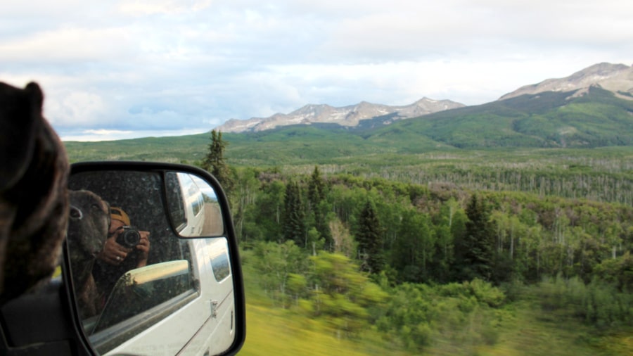 The author Abigail Nueve with her dog taking a picture through the car's sidemirror with a scenic view in Kebler Pass