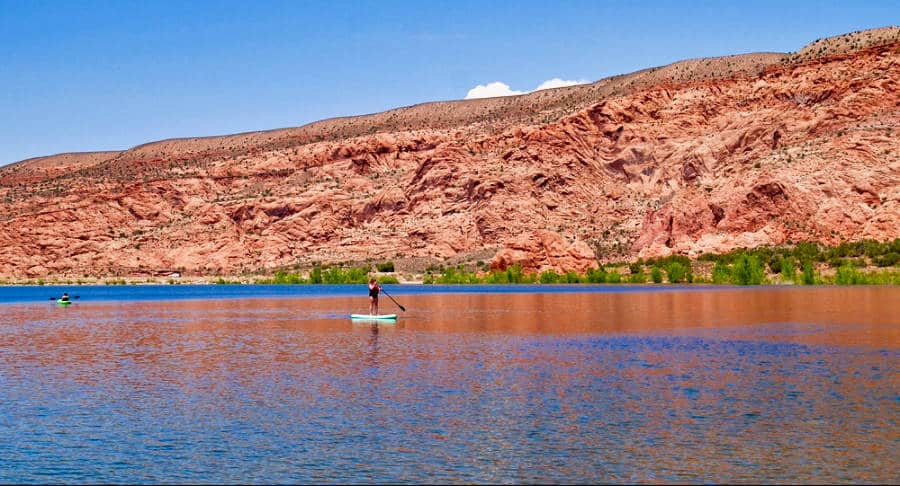 A man paddleboarding in Ken's lake with red rock mountain in the background