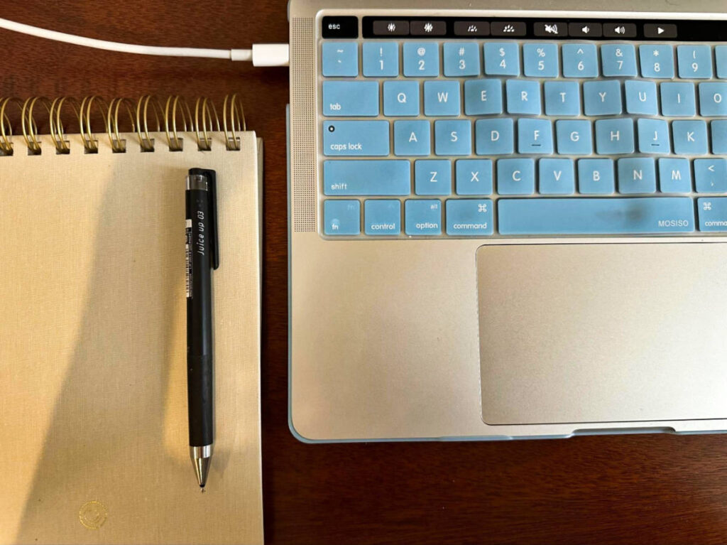 Closeup look of the keyboard of MacBook and a pen on top of the notebook on the wooden table