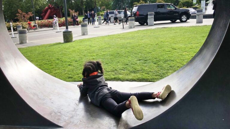 A kid lying inside the round sculpture at the park