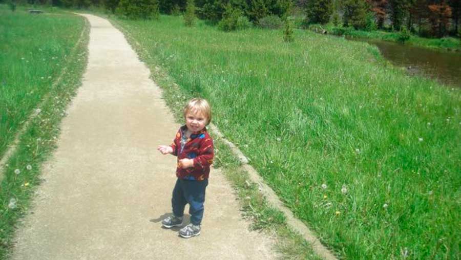 Kid on a walk path surrounded by green grass and dandelions