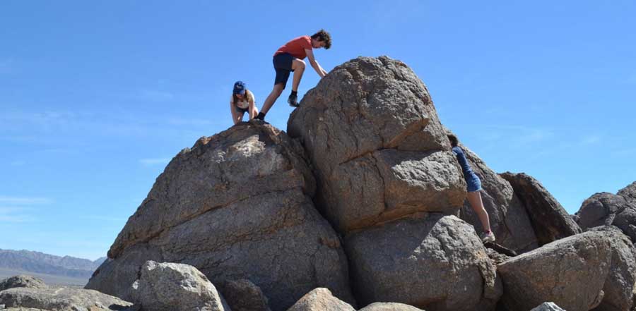 Kids climbing a boulder under the clear blue sky