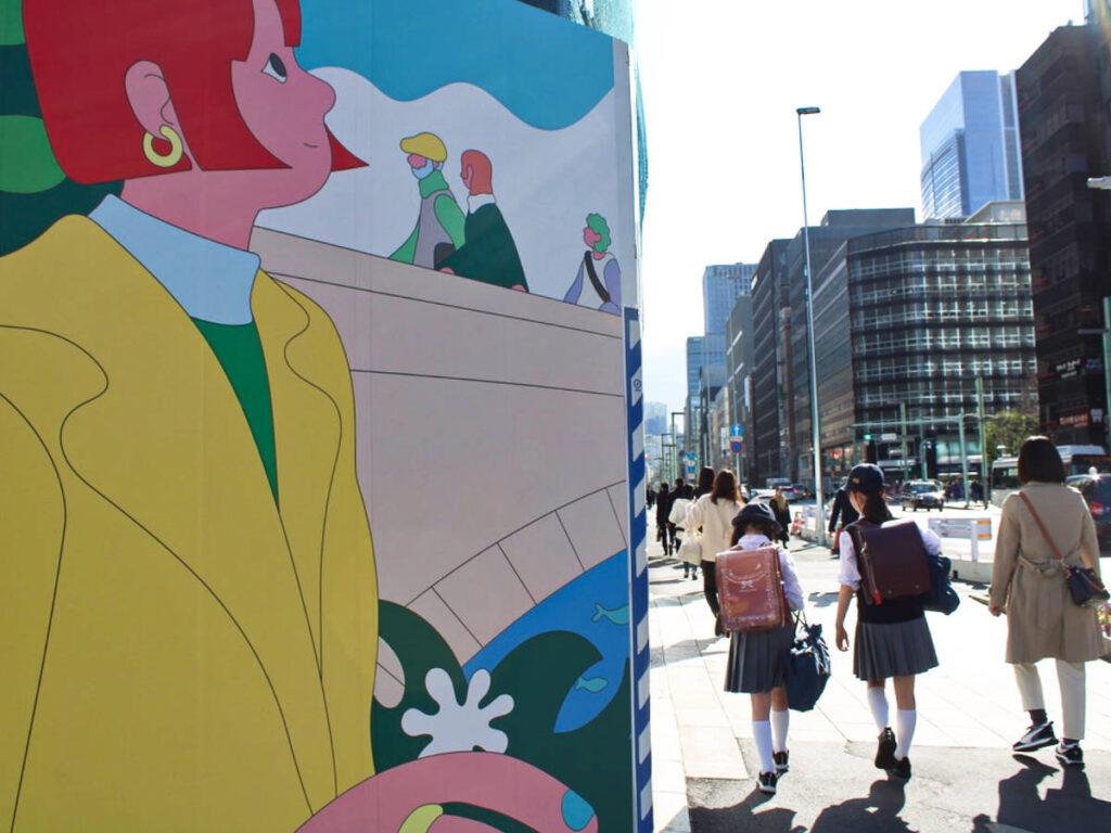 View of the adults and kids walking on the street of Tokyo with a colorful mural on the side