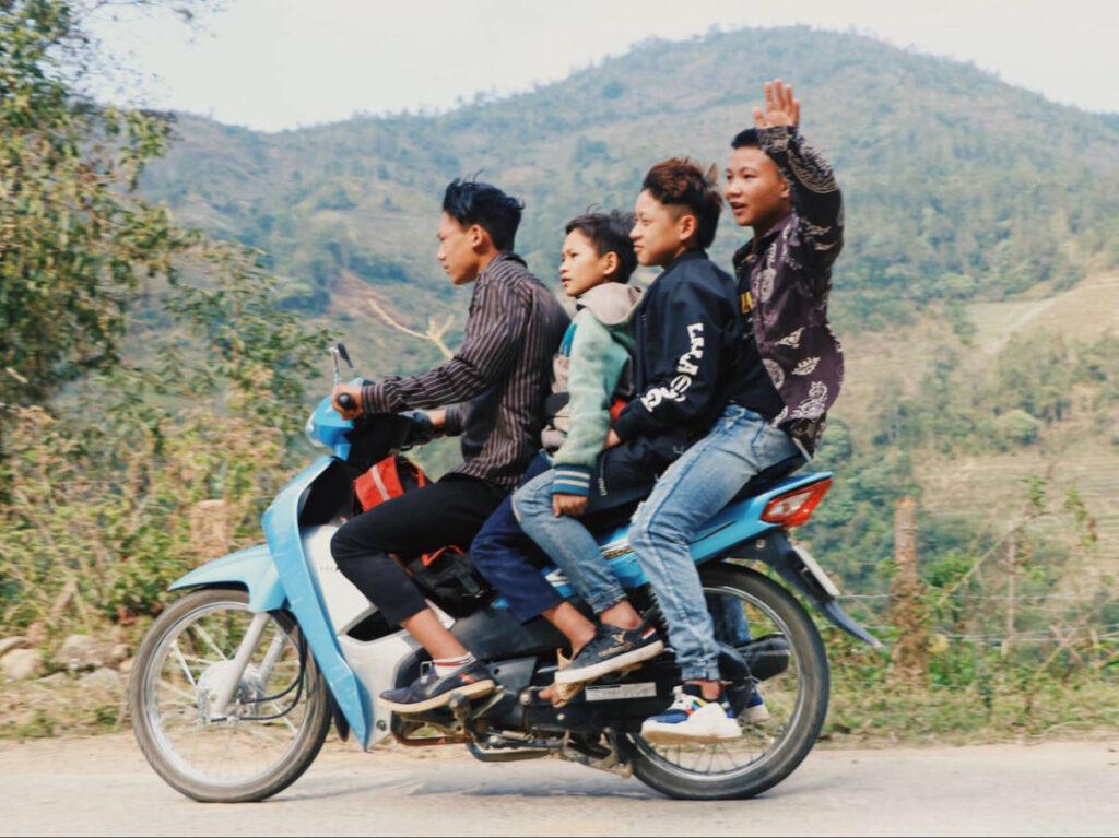 Four people riding on one motorbike with mountain views in the background