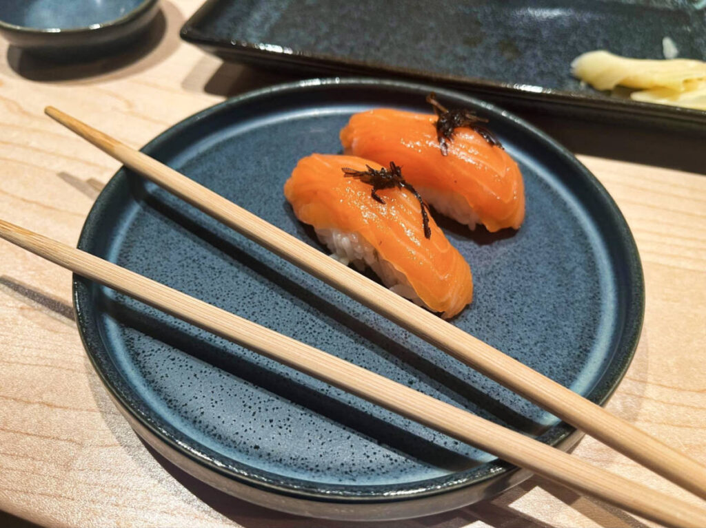 A black round plate with king salmon nigiri and chopsticks from Bondi Sushi