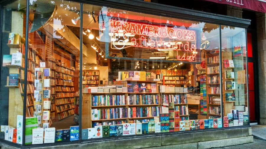 View of the glass paneled Kramerbooks & Afterwords store with illuminated neon lights signage from the outside