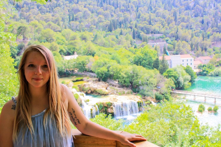 Taylor stands in front of a view of Krka National Park, with boardwalks, lakes, and waterfalls