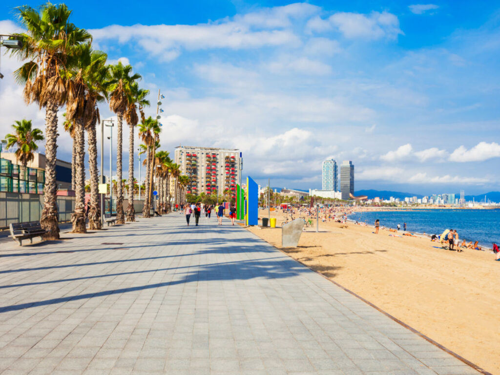 La Barceloneta Beach in Barcelona with palm trees and individuals strolling along the coastline