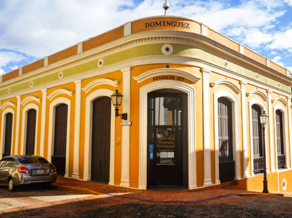 The vibrant yellow exterior of La Botica Museum with a car parked in front of it