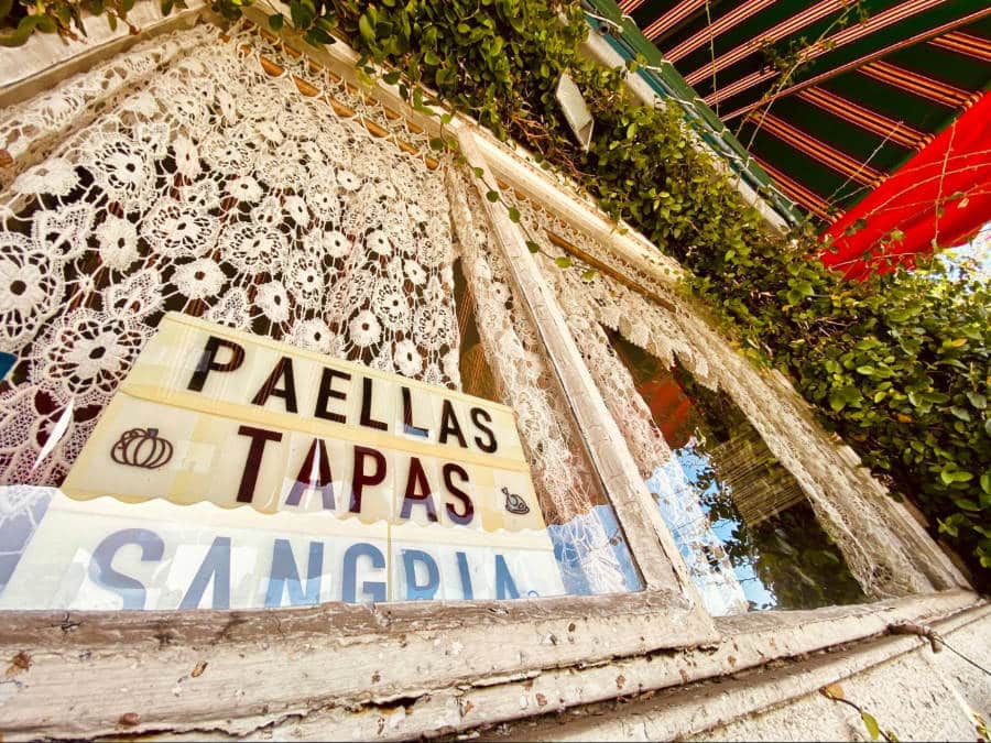 A glass window with lacey curtain view from outside of La Paella