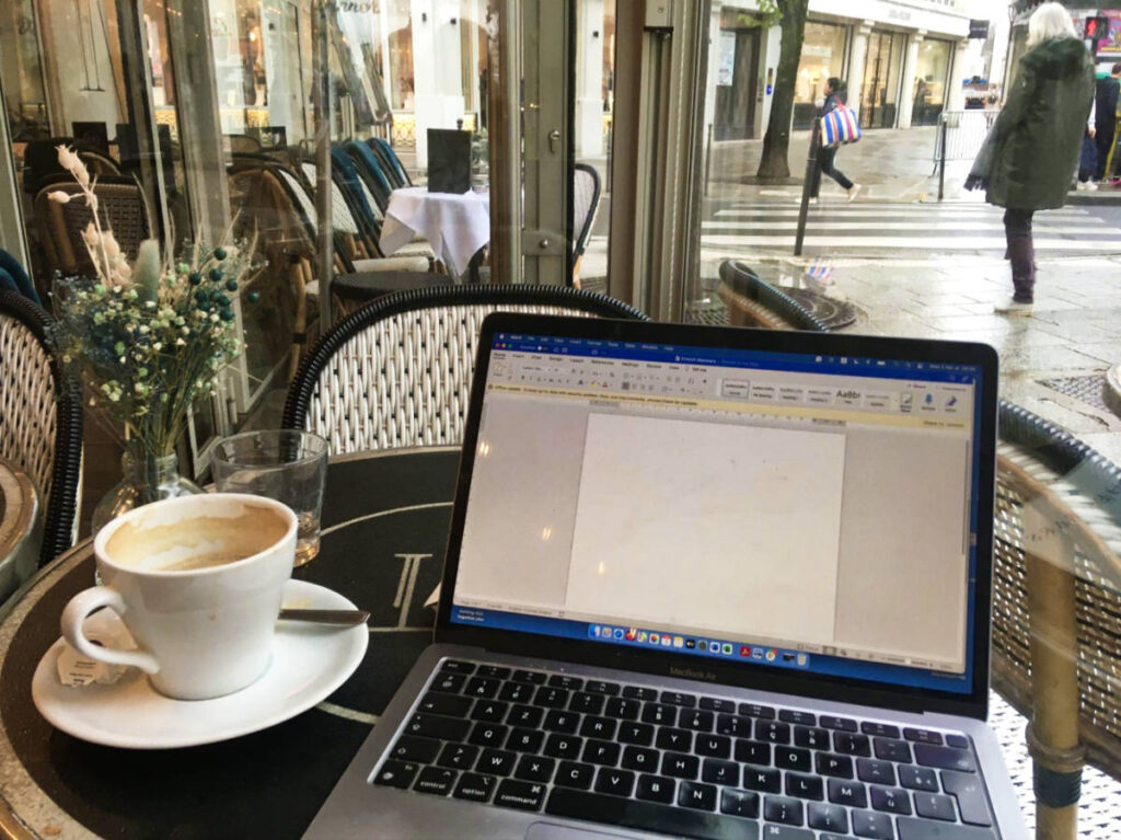 A cup of coffee beside the working laptop inside a cafe