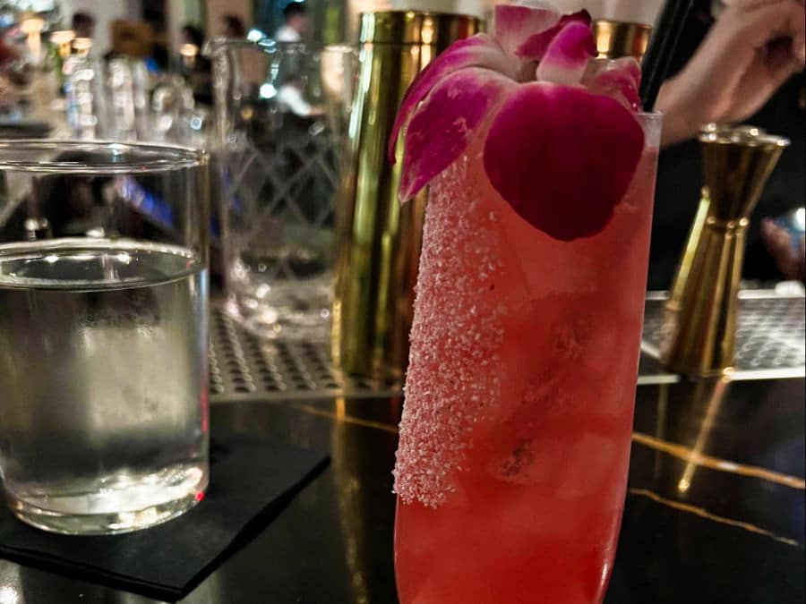 A glass of pink cocktail with a flower on top
