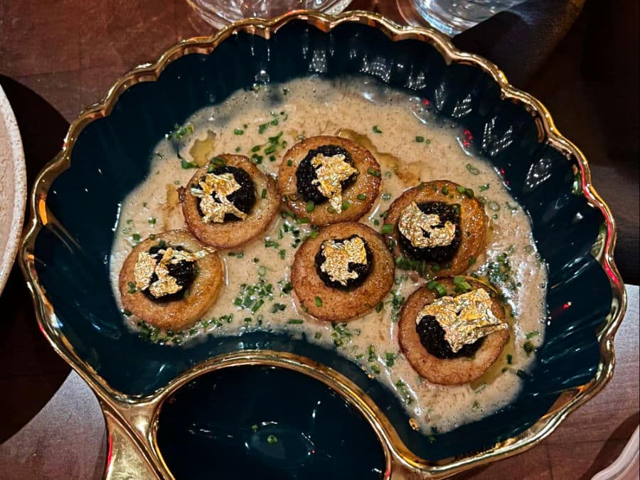 A cream soup with gold flakes on top served on a blue shell shaped ceramic bowl