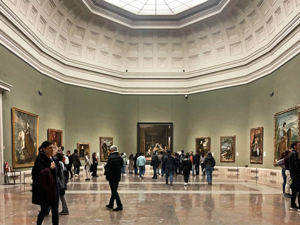People admiring the Las Meninas by Diego Velazquez, displayed inside a museum