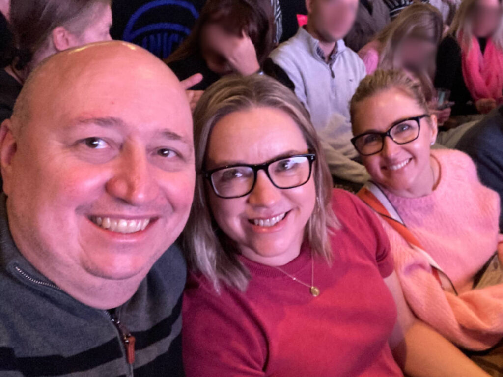 The author Laura Falin with her husband and a friend smiling for a photo while watching the Mean Girls