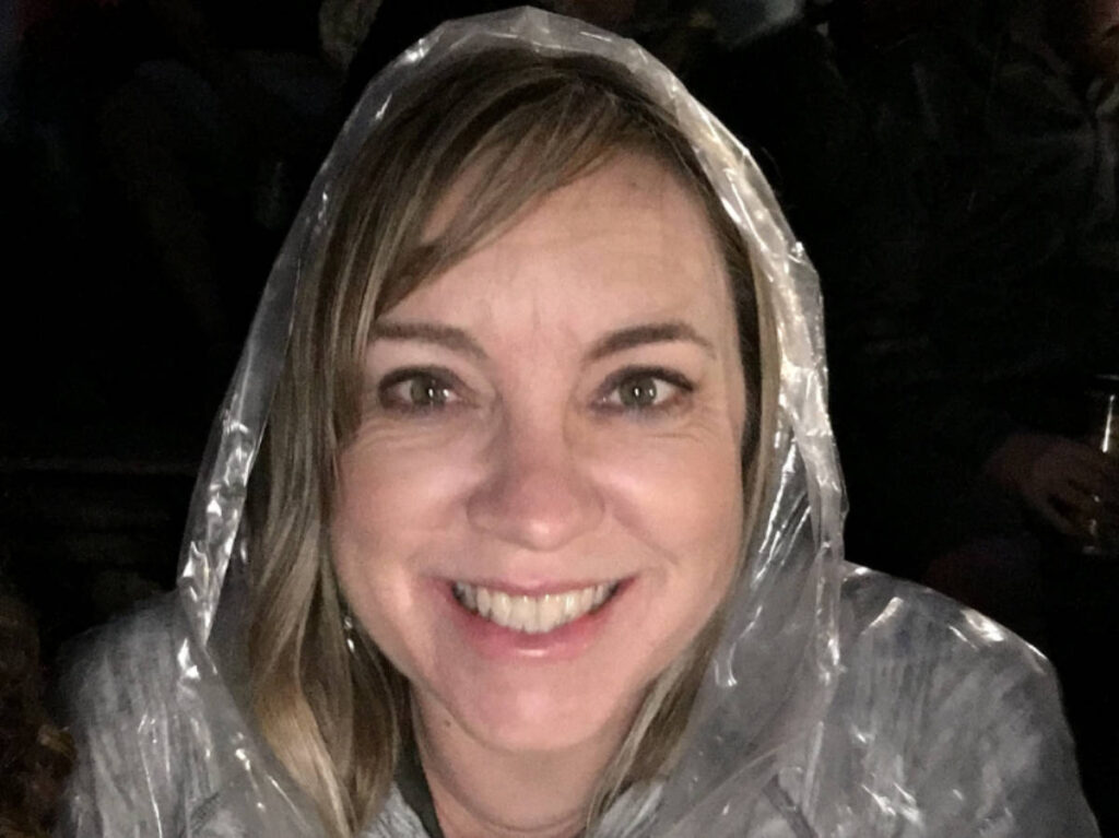 The author, Laura Falin smiling for a selfie while wearing a raincoat during a rainy day