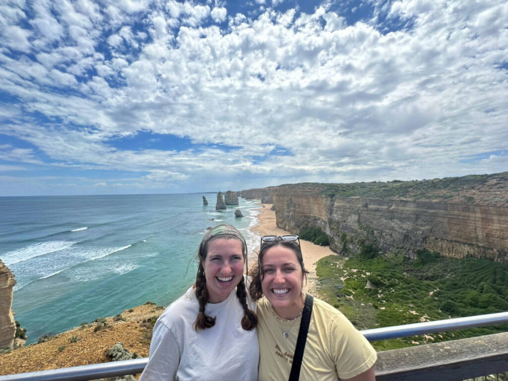 The author Laura McFarland and her partner smiling for a photo with an overlooking view at Great Ocean Road