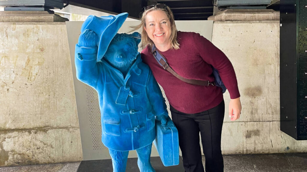 The author Laura smiling for a photo with a Paddington Bear Statue