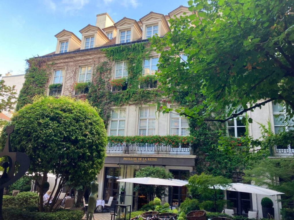 Exterior view of the Le Pavillon de la Reine hotel surrounded by greenery from its courtyard